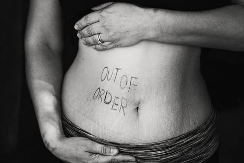 Woman showing stomach w/ words "Out of Order Gut". Leaky Gut. Unhealthy food