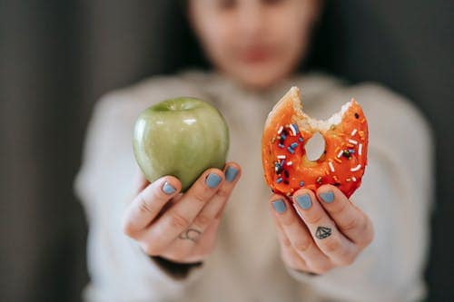 Why are the less healthy food choices typically cheaper? woman holding an apple and a donut. Lifestyle