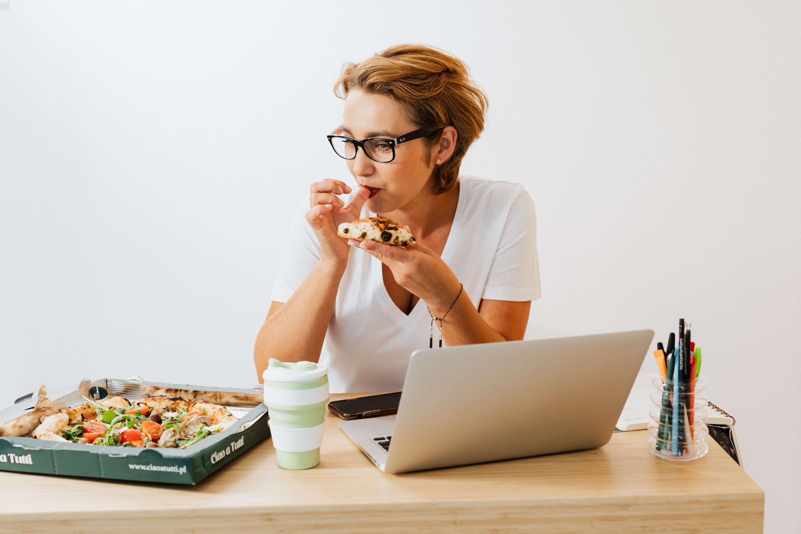 White woman eating pizza at her desk in front of her computer. Does Diet Affect Seborrheic Dermatitis