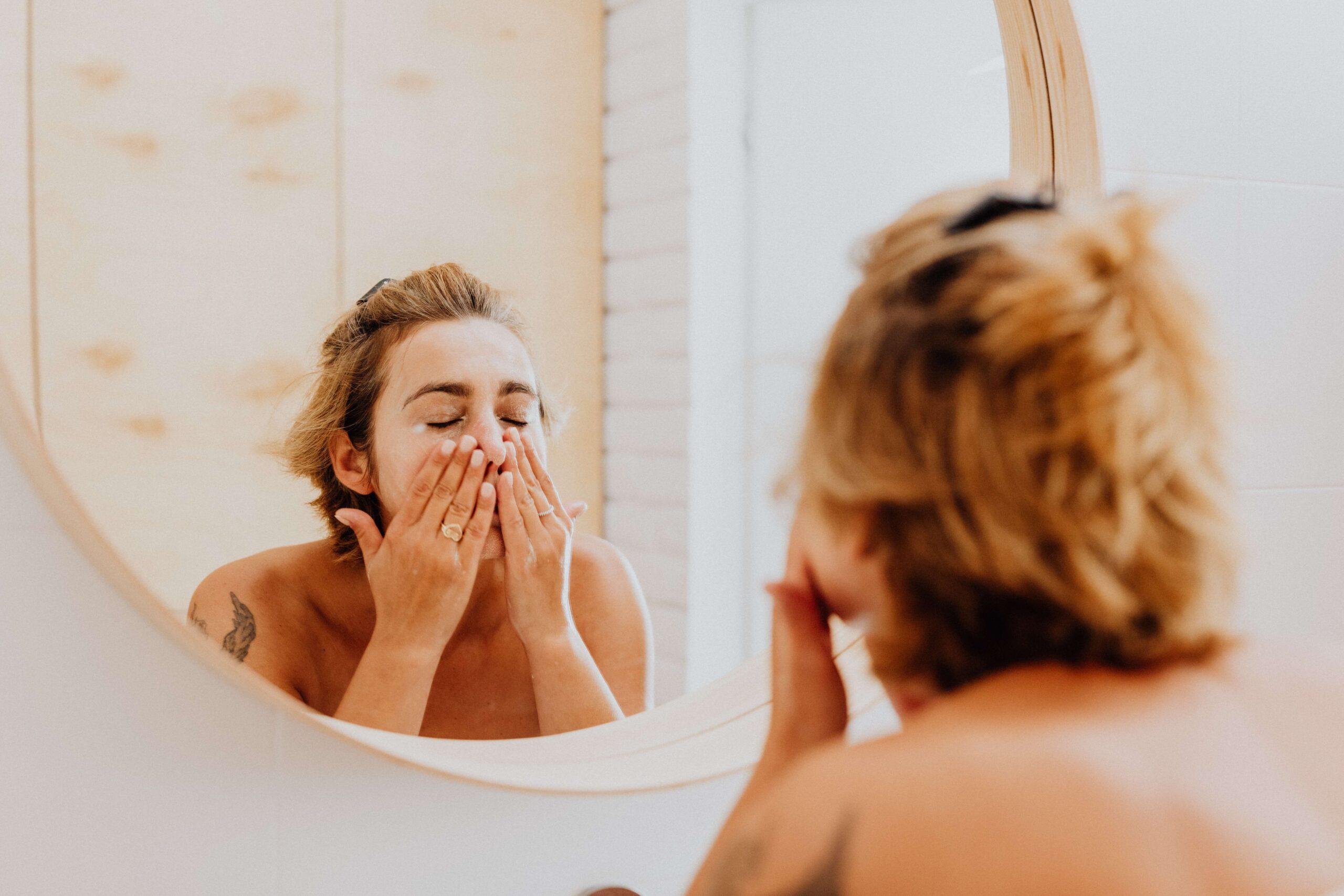 White woman washing her face while in front of the mirror. Seborrheic Dermatitis on Face