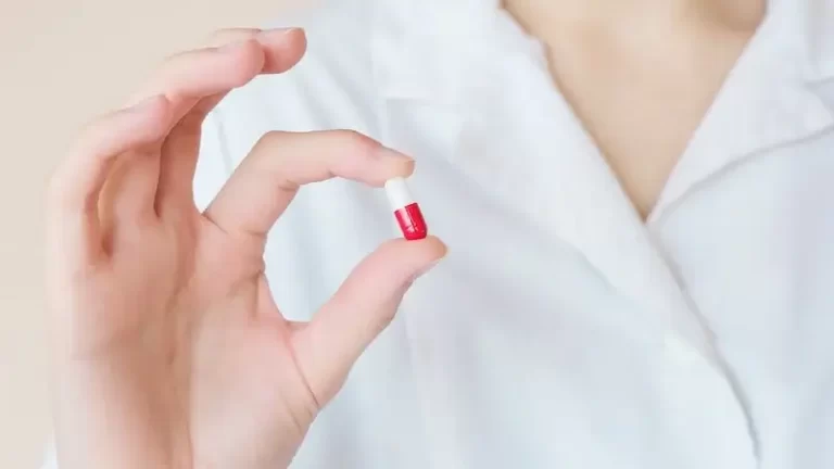 Doctor in white coat holding a white and yellow pill/antibiotics. Do antibiotics affect gut health? Antibiotics