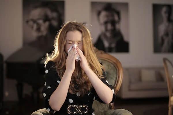 White Woman with red hair sitting in a chair blowing her nose due to allergies.