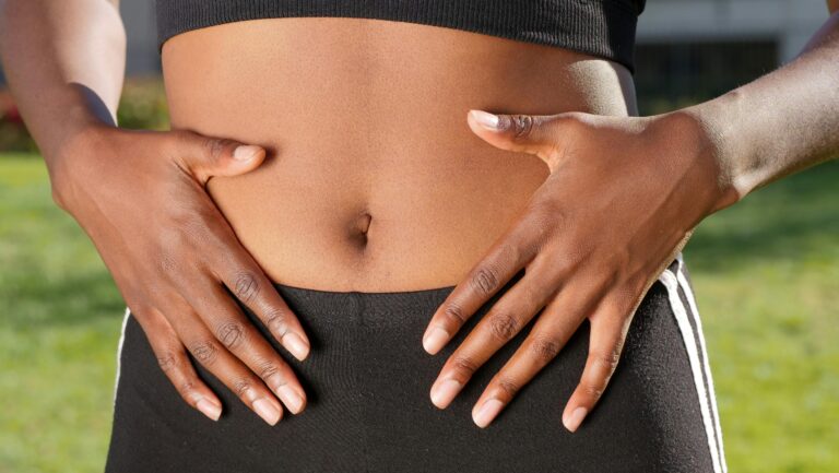 Black woman holding her stomach, wearing workout clothing ( black). She is concerned about "What is gut health diet?"