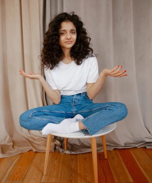 Young white woman with dark hair, wearing jeans and a t-shirt, sitting on a stool. Asking the question, " Is Gut Health Important?"